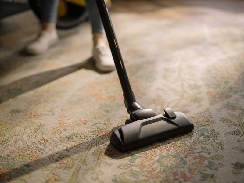 A Lenuma professional vacuuming a patterned rug, showing careful and thorough home cleaning for a fresh, cared-for living space.